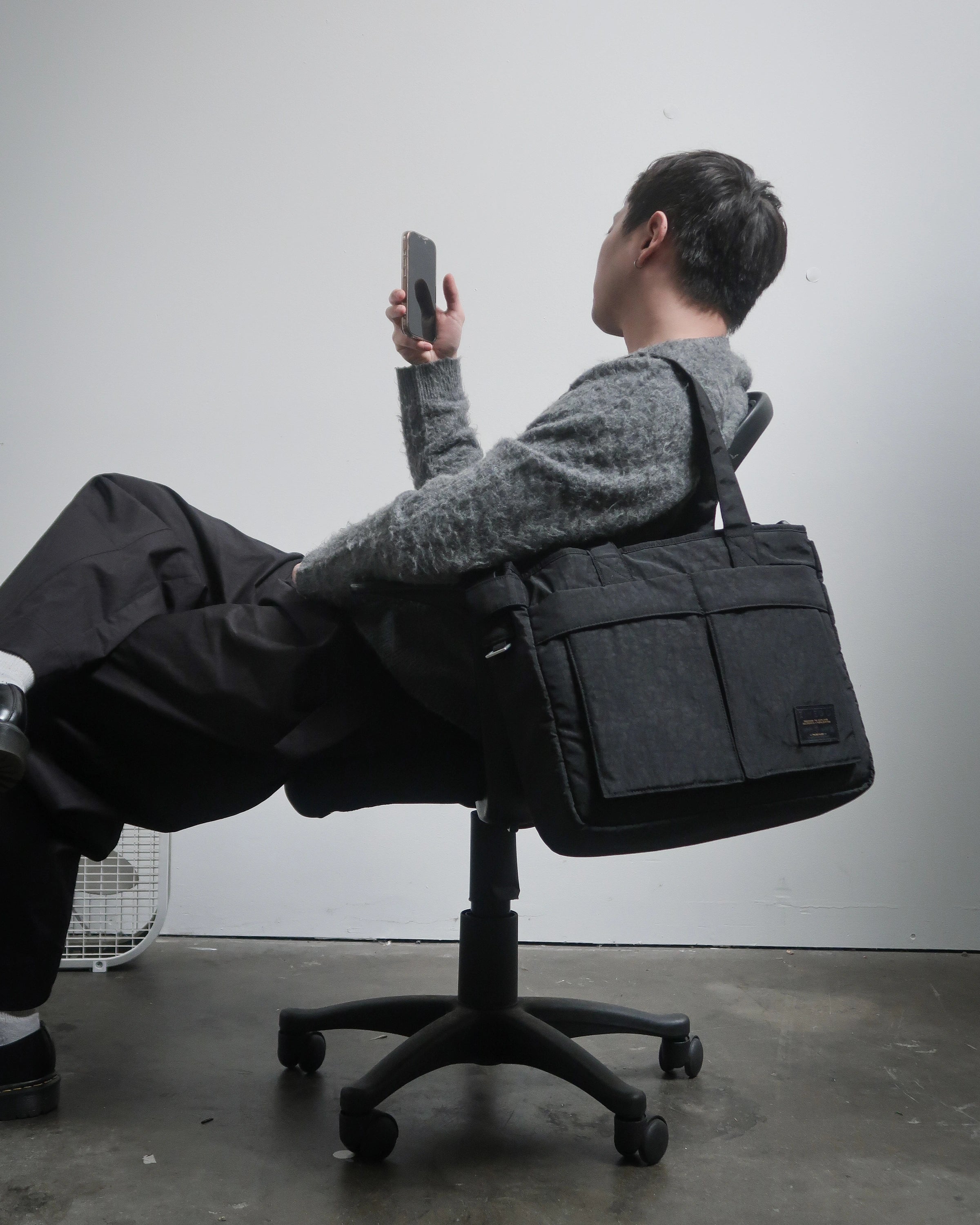 Person sitting on a chair with a large black bag over their shoulders against a plain background