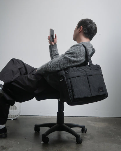 Person sitting on a chair with a large black bag over their shoulders against a plain background